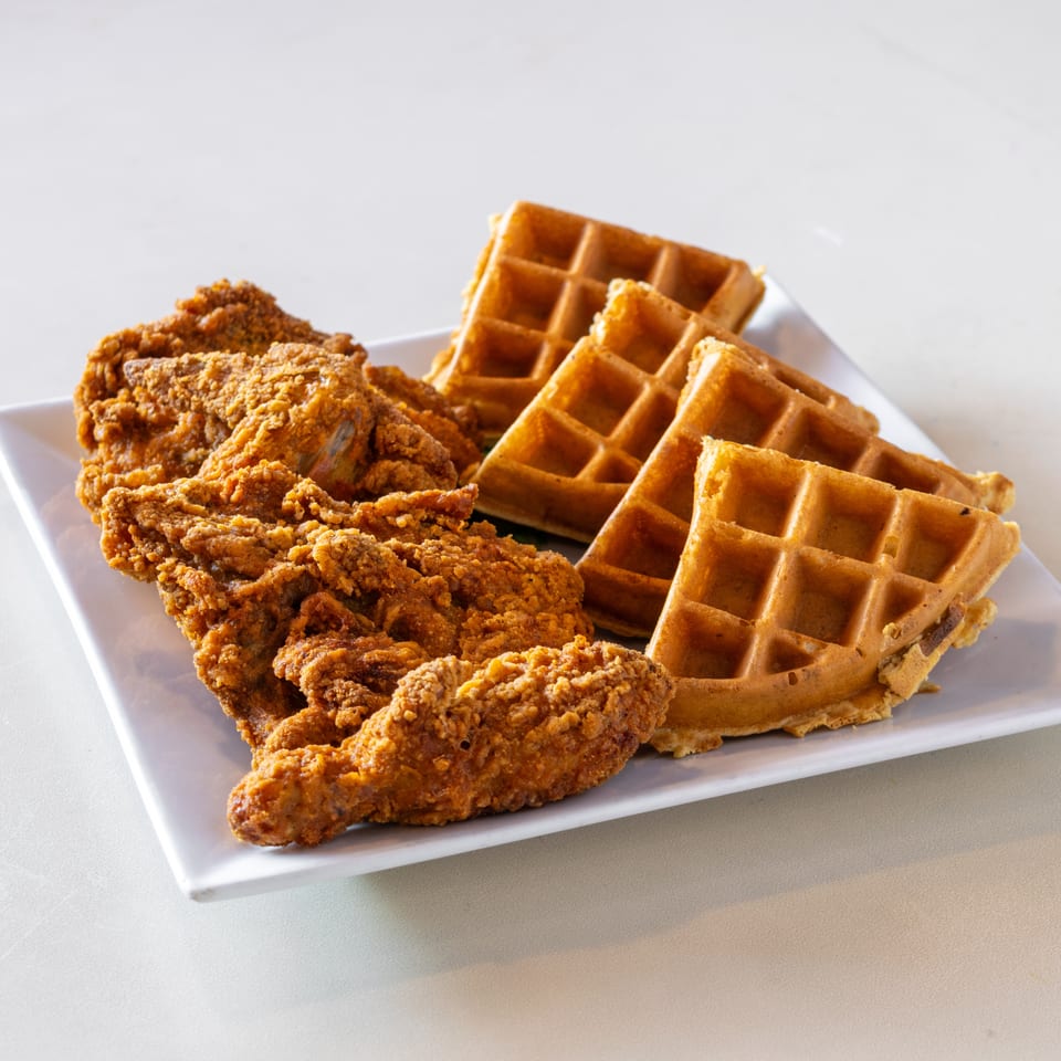 Crispy fried chicken and golden waffles arranged on a white rectangular plate.