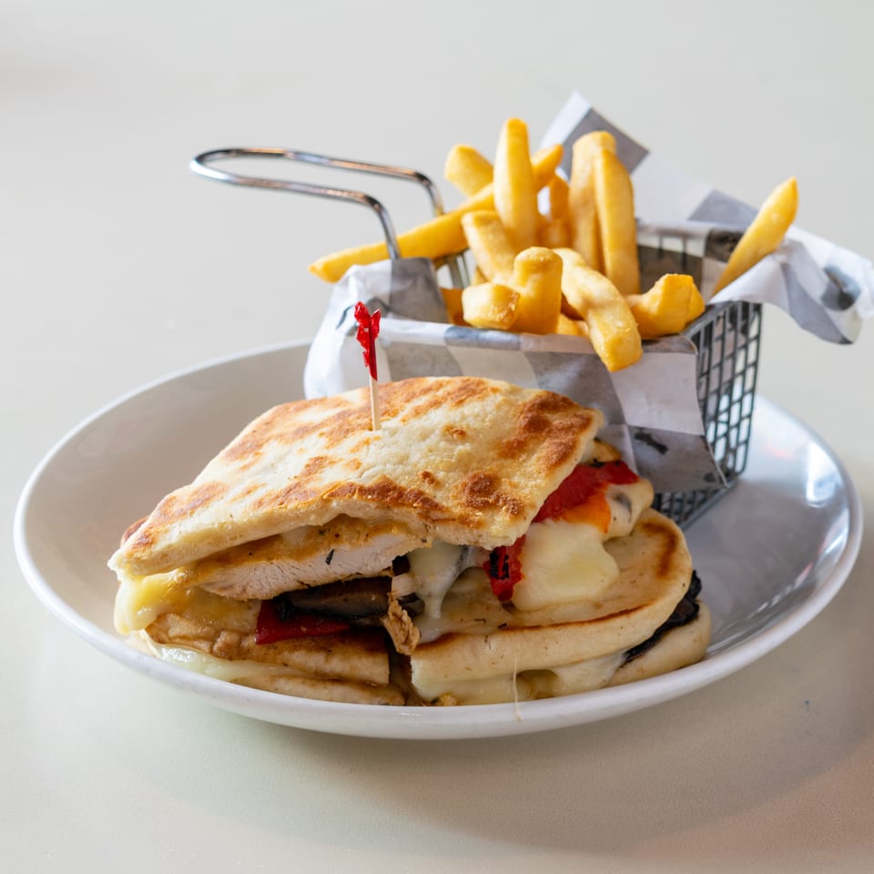 Grilled chicken and cheese sandwiches with roasted peppers, served alongside golden fries in a lined basket.